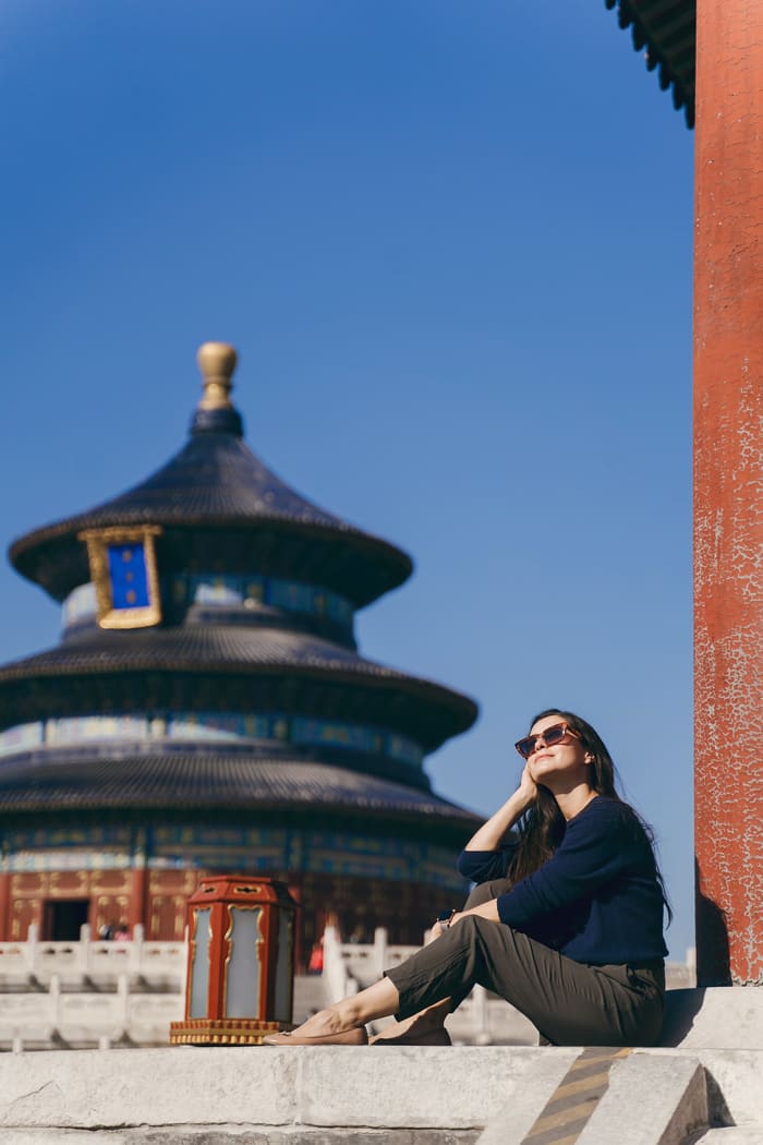 mujer sentada posando para la foto en su viaje a beijing detrás un edificio