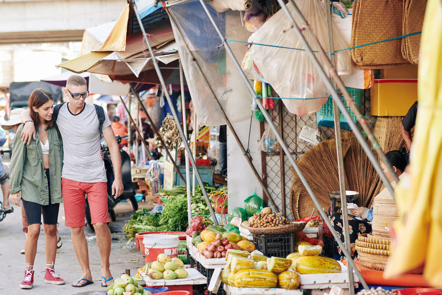 una pareja de hombre y mujer en un mercado chino donde venden variedad de frutas y verduras y mas cosas