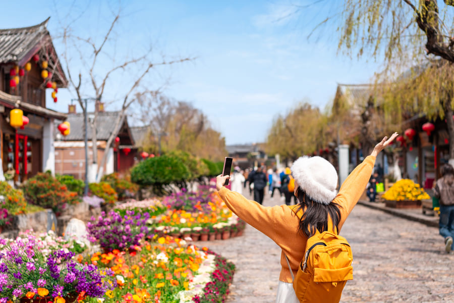 mujer feliz con un suéter amarillo y un paisaje con flores, árboles y casas en Yunnan China